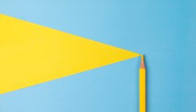Yellow colored pencil with an illustration of a yellow triangle coming from the top left tip on a light blue background